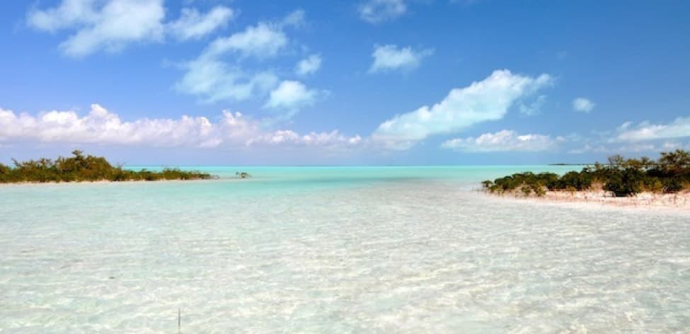 A fly angler wading a vast white-sand bonefish flat under a dramatic sky